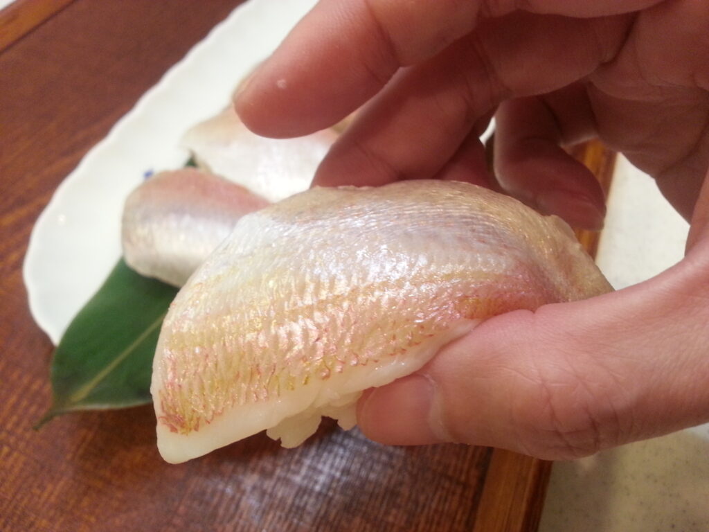 「小鯛ささ漬」で作ったにぎり鮨を指でつまんで食べる様子